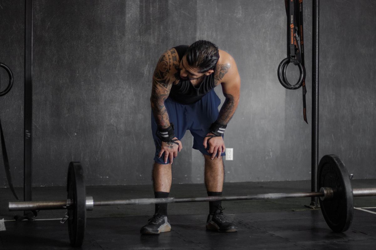 Gym plateau: a practical checklist to restart progress | the gym pro Lifter Resting With Hands On Knees Beside A Barbell